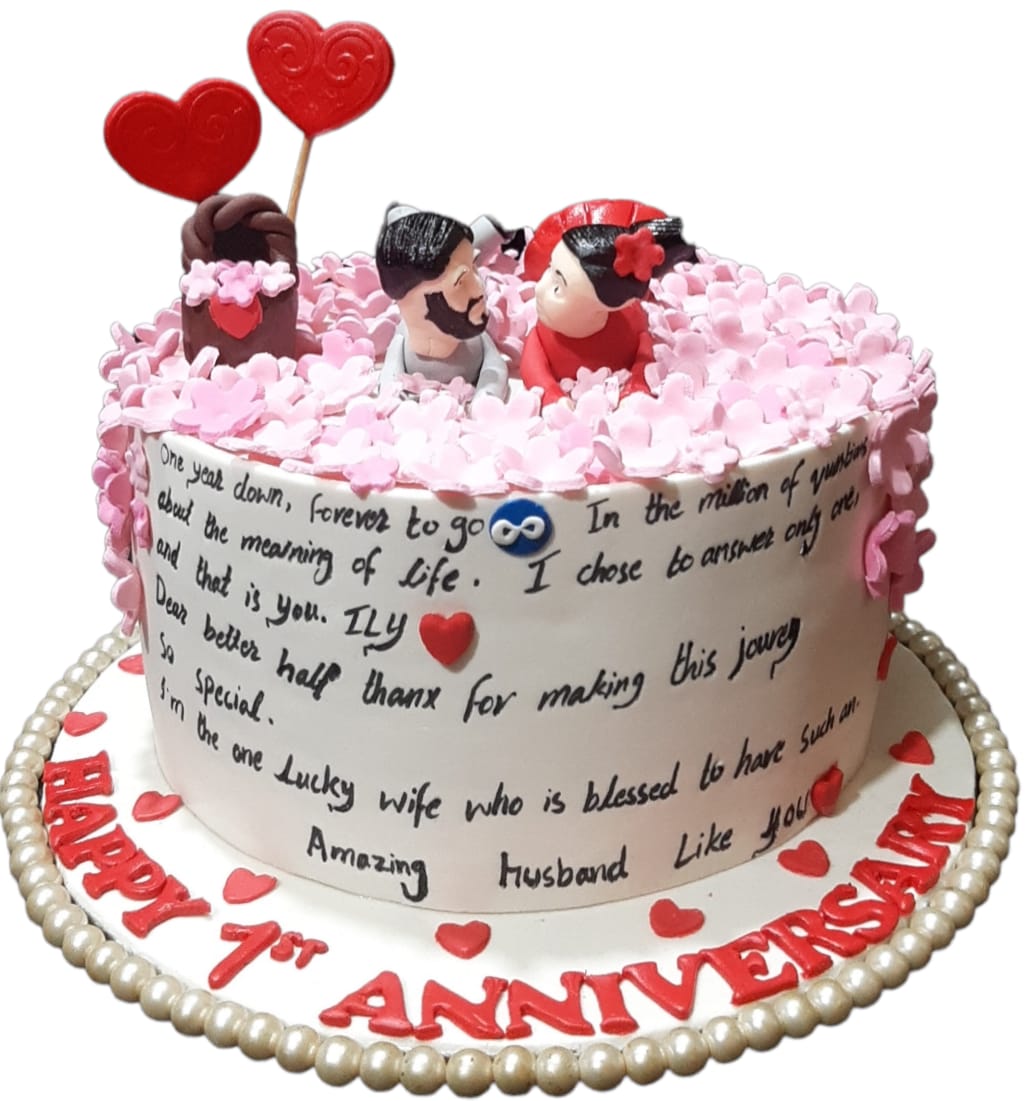 Happy 1st Anniversary white cream love letter cake with pink blossoms, couple figurines and red heart lollipop toppers by Marbella Cakes
