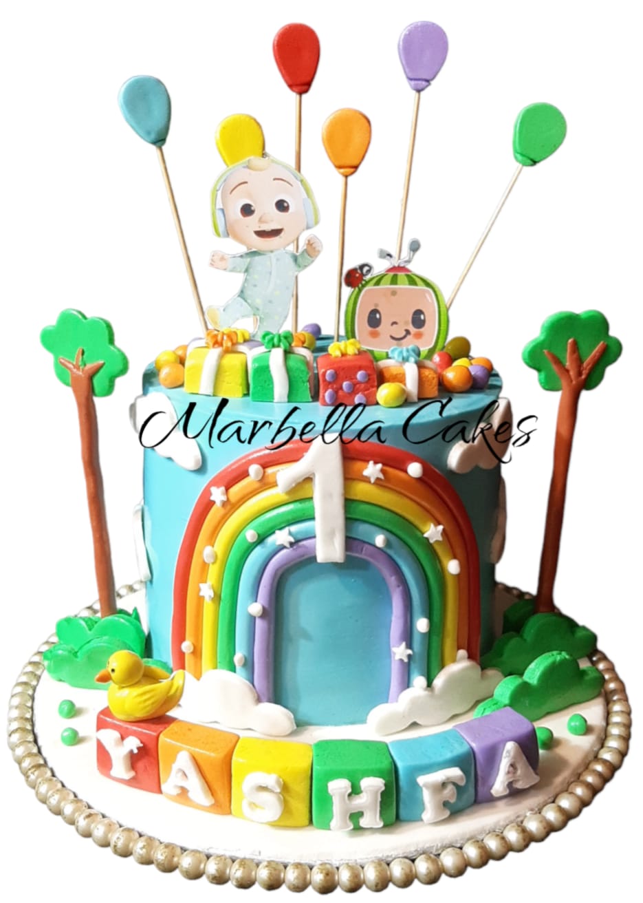 CoComelon Rainbow and Balloons Birthday Cake with blue buttercream, rainbow arch, JJ and CoComelon character cutouts, colourful balloon sticks, tree toppers and alphabet block name letters on board