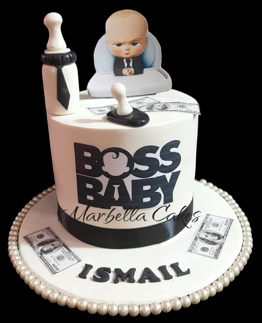 Boss Baby single-tier white fondant cake with black BOSS BABY logo wrap, edible character cutout topper, fondant baby bottle, pacifier, dollar bill props and pearl-beaded board with personalized name