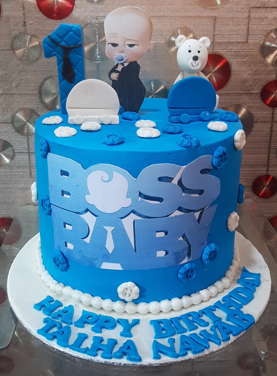 Boss Baby royal blue single-tier 1st birthday cake with quilted number 1 topper, Boss Baby and white teddy bear fondant figurines, blue BOSS BABY logo lettering and personalized name board