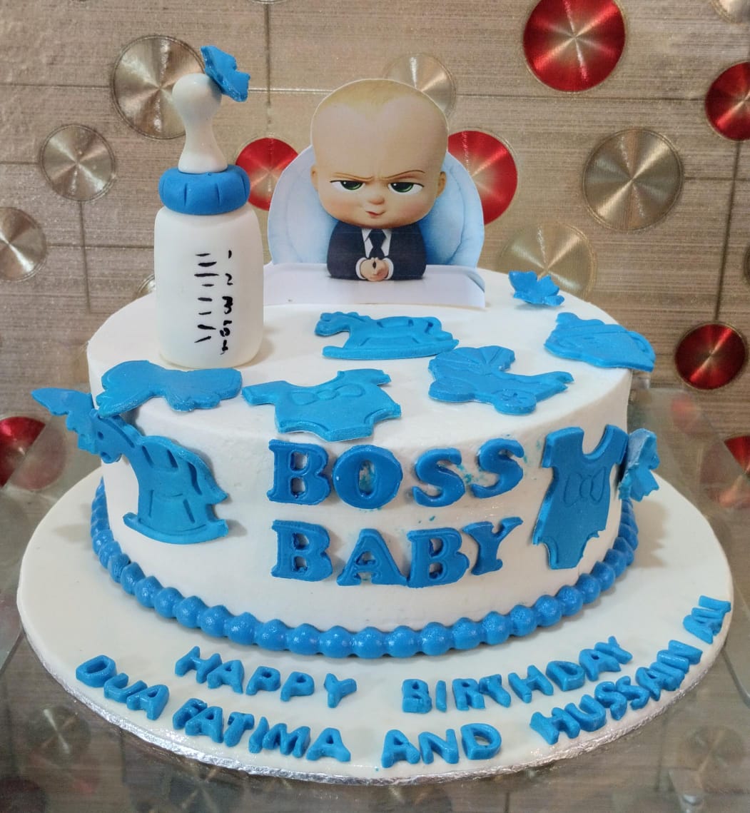 Boss Baby single-tier white and blue fondant cake with character topper, baby bottle, and blue baby clothes decorations