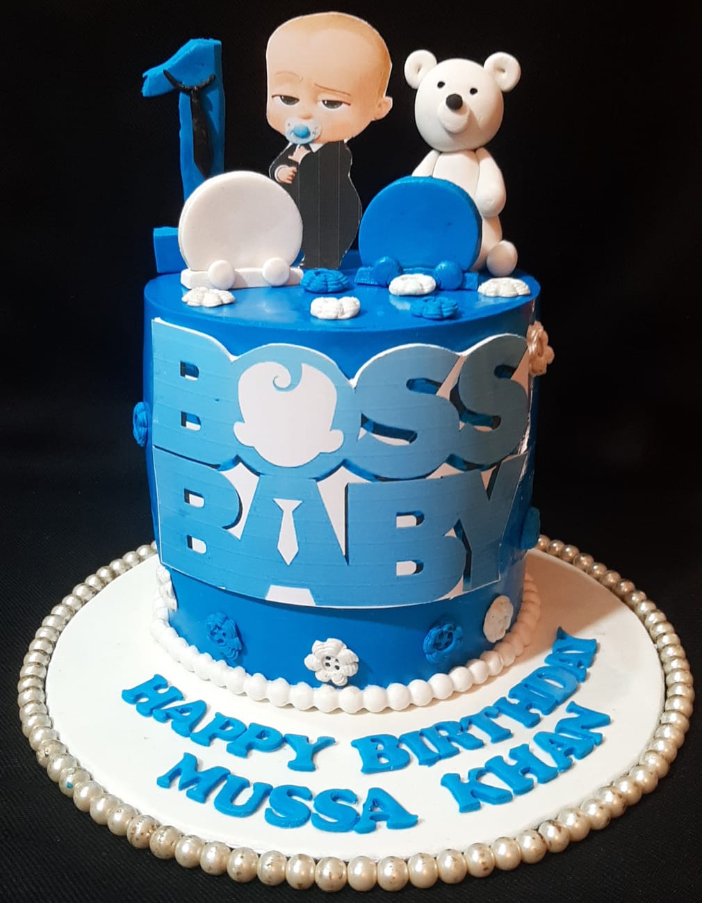 Boss Baby 1st birthday single-tier royal blue fondant cake with character topper, white teddy bear, and number 1 topper