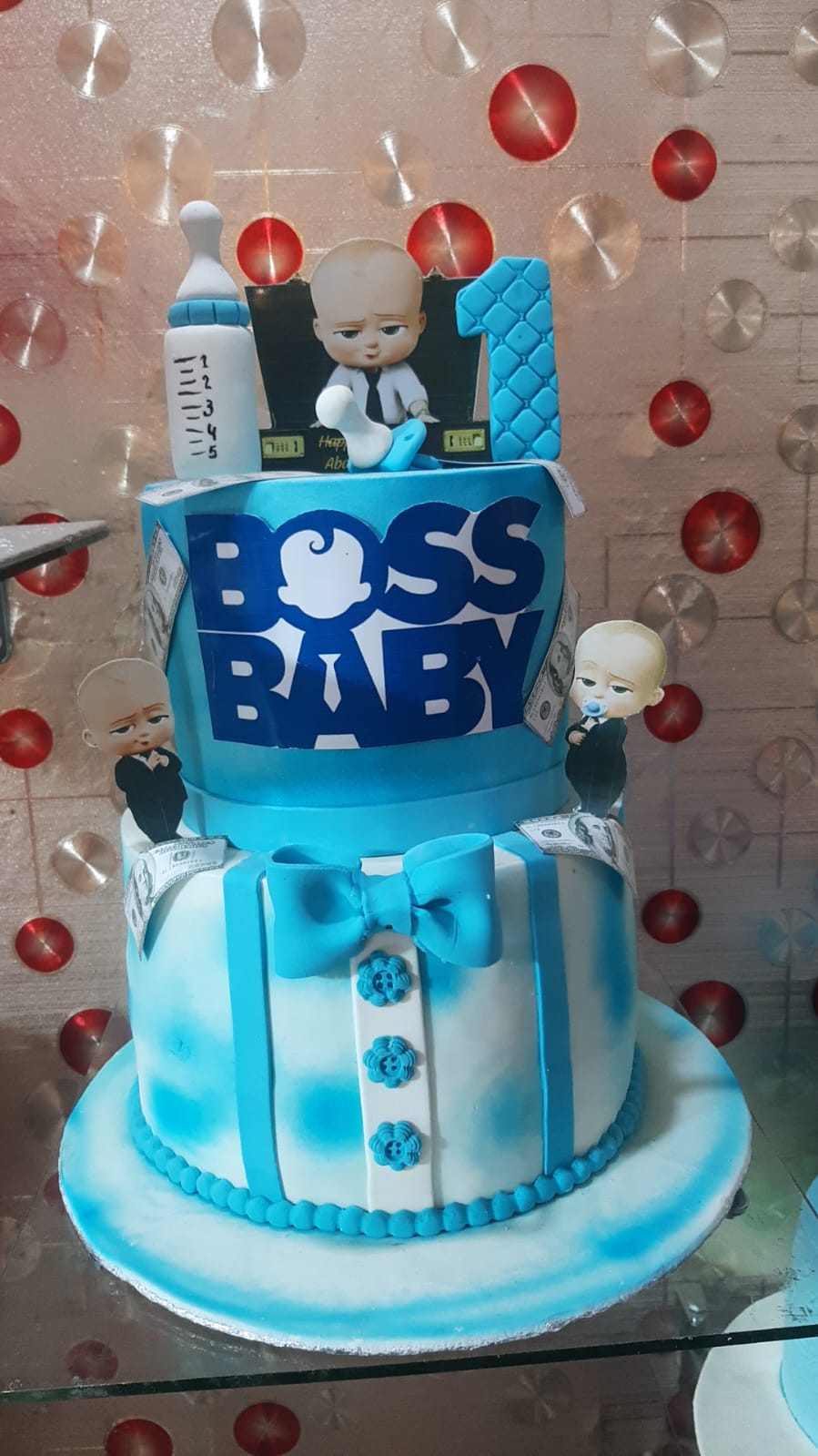 Boss Baby 2-tier blue and white fondant birthday cake with character figurines, money stacks, and suit design