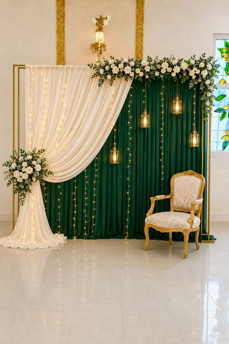 Elegant emerald green velvet and white sheer floral backdrop with gold lanterns, fairy lights and accent chair