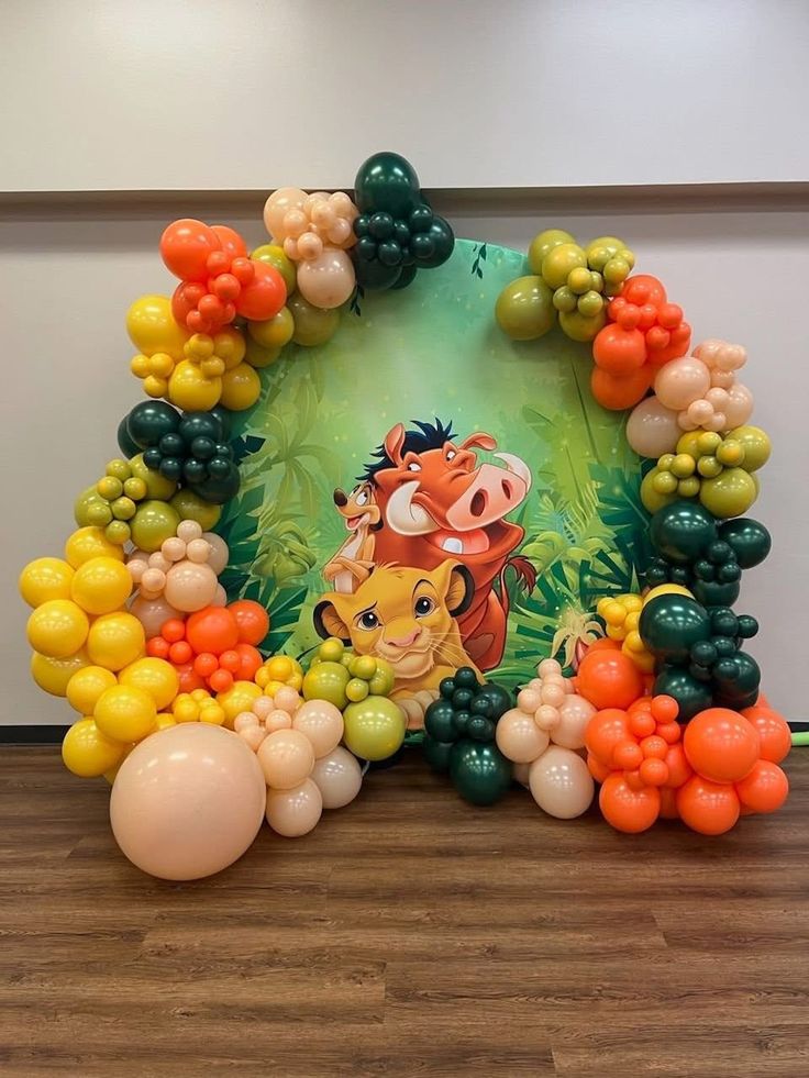 Lion King birthday decoration with yellow orange green balloon arch and Simba Timon Pumbaa jungle backdrop
