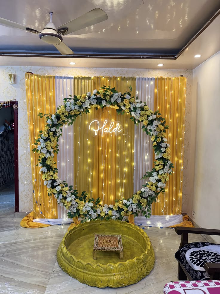 Haldi ceremony decoration with yellow white floral ring, Haldi neon sign, golden drape backdrop with fairy lights and traditional thaal