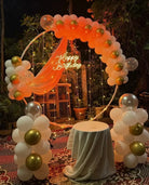 Outdoor birthday decoration with peach white gold balloon ring arch, Happy Birthday neon sign, fairy lights and balloon columns