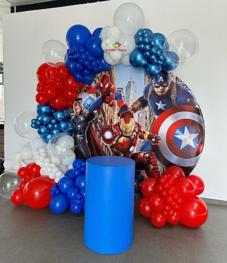 Avengers birthday decoration with circular backdrop featuring Iron Man Thor Spider-Man Captain America, red blue white balloon garland and blue cake cylinder