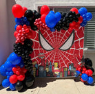 Spider-Man birthday decoration with red black blue balloon garland arch and Spider-Man spiderweb mask backdrop with city skyline and comic pop art accents