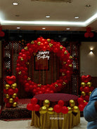 Red and gold balloon ring arch birthday decoration with Happy Birthday neon sign, heart foil balloon columns and gold draped cake table