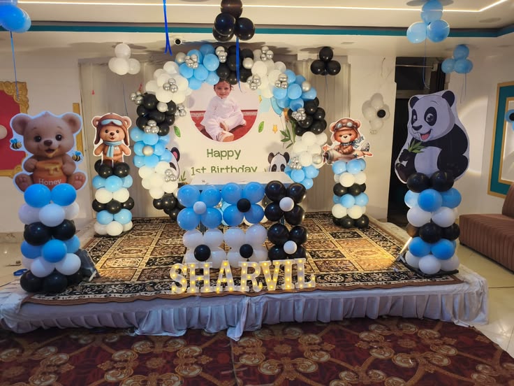 Panda and teddy bear 1st birthday stage decoration with blue black white balloon ring arch, custom photo backdrop, large panda cutout standees and illuminated marquee name letters