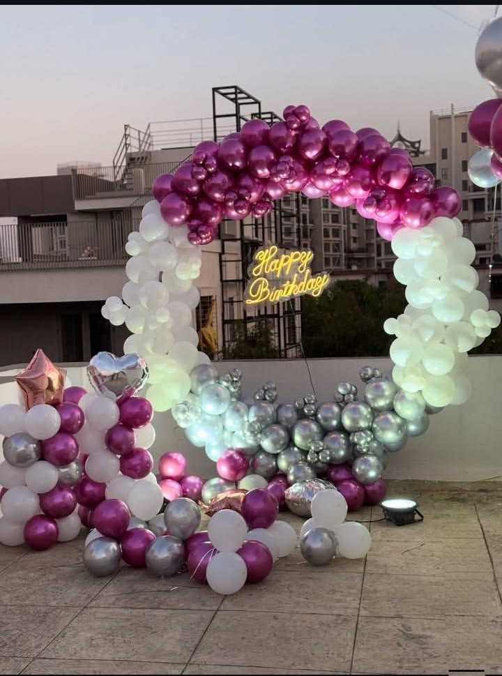Magenta and silver outdoor birthday balloon ring arch decoration with chrome fuchsia silver white balloons, Happy Birthday neon sign and heart foil balloons at dusk