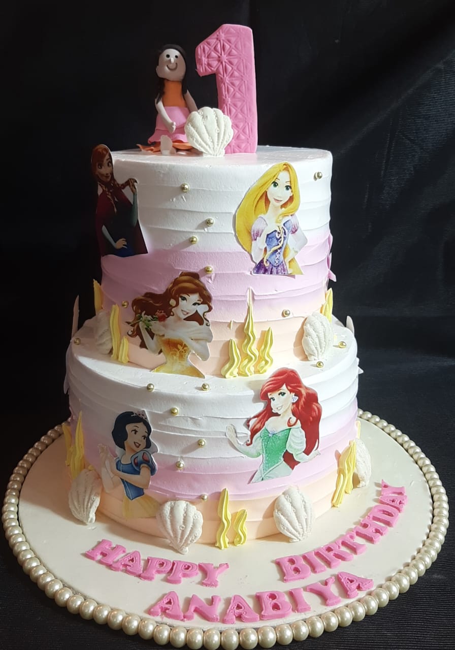 Disney Princess 3-tier pink ombre buttercream birthday cake with edible Ariel Belle Rapunzel Anna Snow White and Moana character cutouts, seashell accents, pink number topper and personalized Happy Birthday name on base
