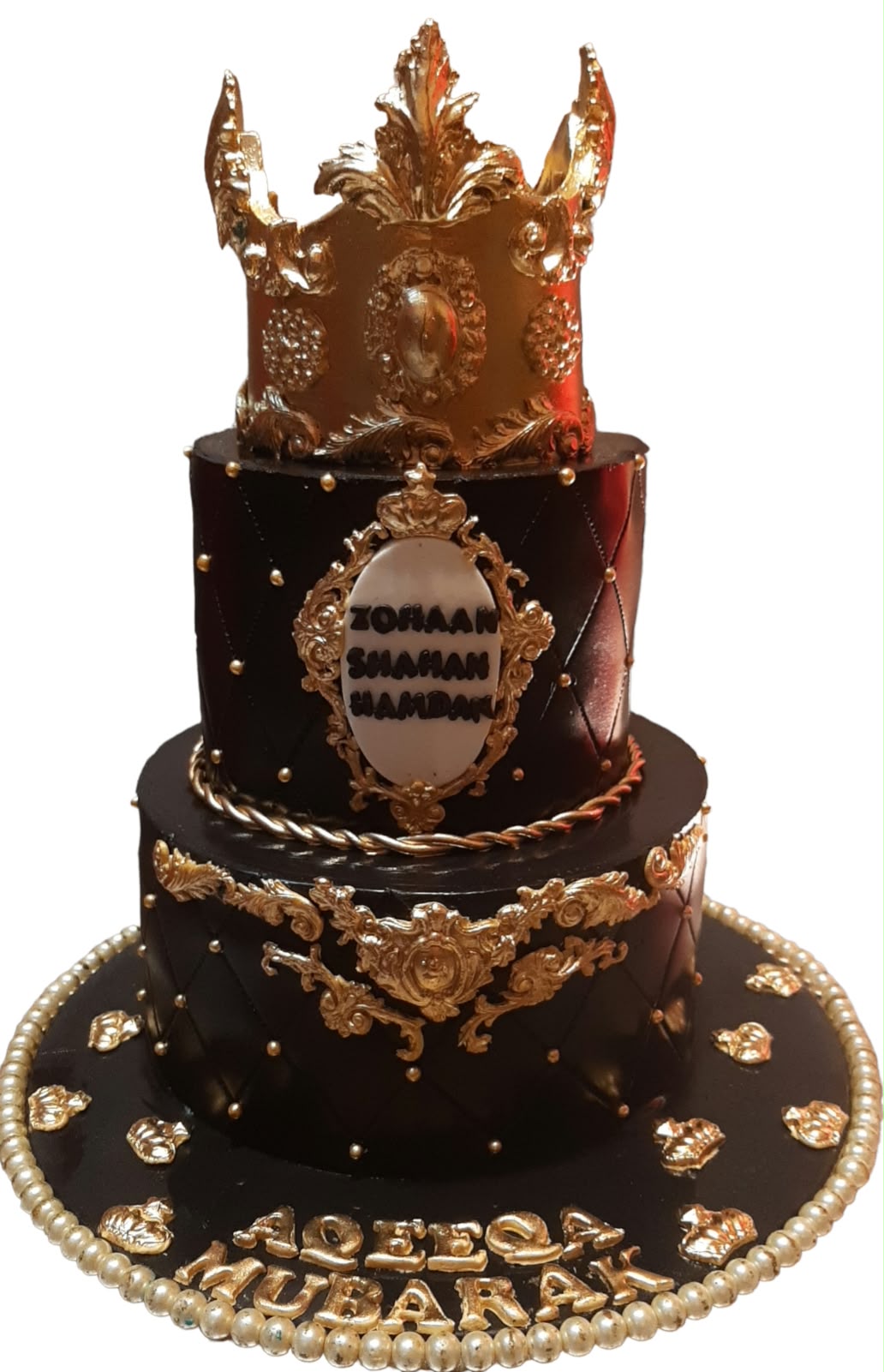 Royal black and gold 3-tier luxury birthday cake with towering gold baroque crown topper, quilted diamond pattern, gold oval name plaque, baroque scroll ornaments and pearl bead border on base
