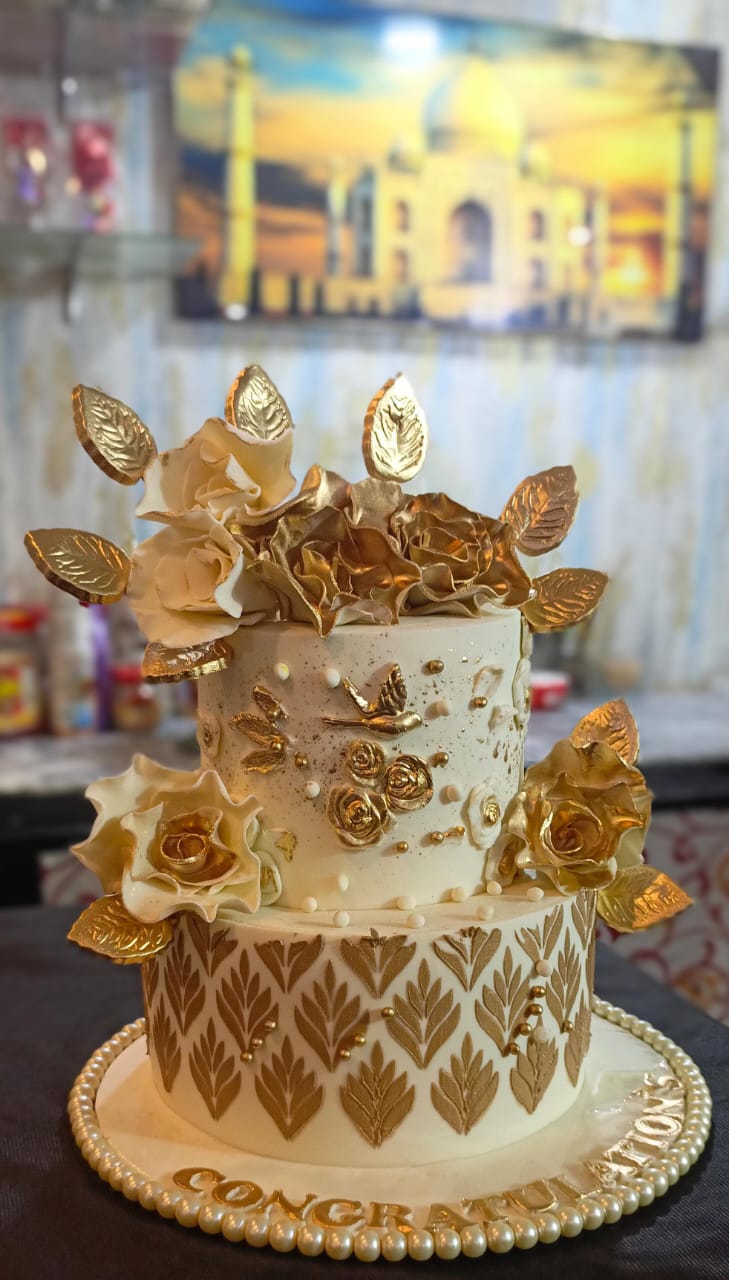 Ivory and gold 2-tier congratulations cake with cascading gold rose bouquet topper, large gold leaf accents, gold damask stencil pattern on bottom tier, gold bird accent and pearl bead border with Congratulations lettering on base