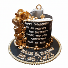 Black and gold engagement cake with white message, gold sugar flowers, ring box topper and Zaib & Bano name plaques on white background
