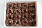 12 chocolate glazed donuts with rainbow sprinkles in white box on white background
