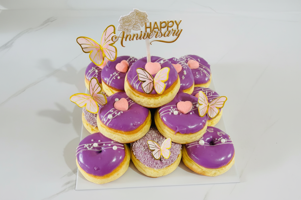 Happy Anniversary purple donut tower with butterfly decorations and gold topper on white background